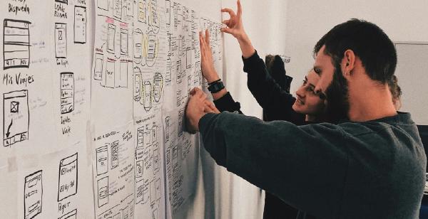 Two people collaborating on hand-drawn UI wireframes taped to a wall