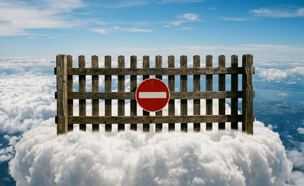 A weathered wooden fence standing on a bank of clouds against a blue sky, a red no-entry sign mounted at its center, open sky on either side